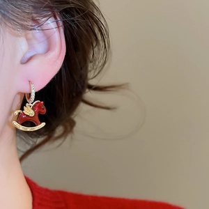 Détail de boucle d'oreille cheval à bascule rouge avec ailes dorées et zircons