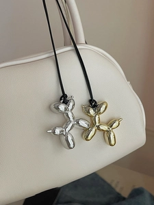 Close-up of metallic balloon dog pendants in gold and silver finish on a stylish handbag