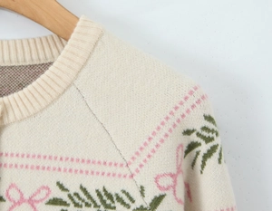 Detail of cream knit cardigan with pink bow and green leaf jacquard pattern