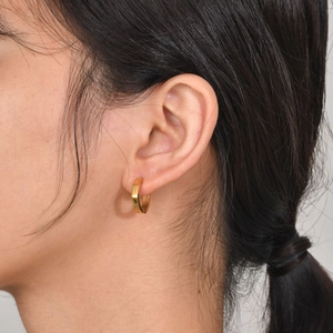 Close-up of golden octagonal huggie hoop earrings worn on ear in a minimalist style