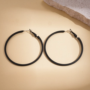 Detail shot of large matte black geometric leather hoop earrings on a beige surface