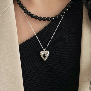 Close-up of a layered 925 silver heart pendant necklace with black beaded chain on a model