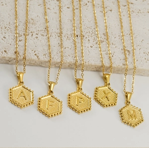 Detailed macro view of 18K gold hexagon initial pendants with beaded edge texture