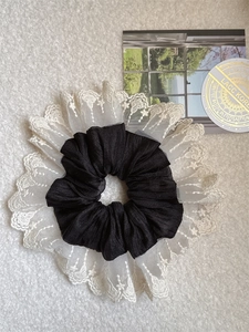 Detail of elegant black fabric scrunchie with layered white mesh lace edging on soft background