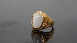 Macro shot of gold ring featuring a large white oval gemstone with cat eye luster