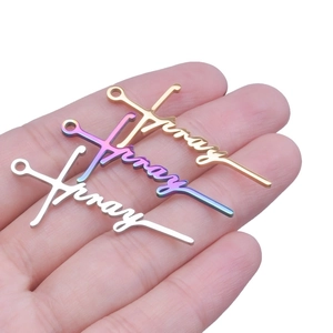 Detailed view of three 304 stainless steel 'Pray' cross pendants in hand, gold and silver