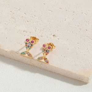Close-up of golden fish earrings inlaid with colorful zircons on marble base