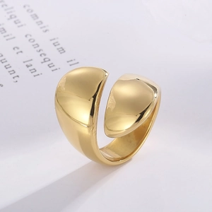 Detailed view of a wide gold-plated open ring with polished finish on artistic background