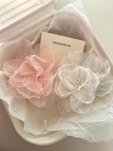 Detailed macro view of white and pink layered mesh camellia flower hair clips in a box
