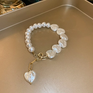 Detail of elegant pearl bracelet with heart-shaped pendants and golden OT toggle clasp