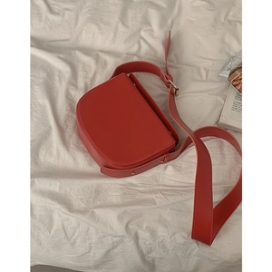 Classic red PU leather saddle bag with wide shoulder strap on white fabric background