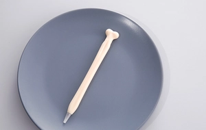 Macro detail of a bone-shaped creative ballpoint pen on a gray minimalist circular tray