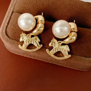Boucles d'oreilles cheval à bascule dorées avec perles blanches sur boîte velours