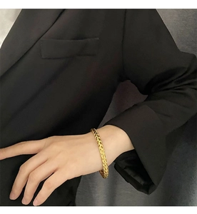 Chic golden woven titanium steel bracelet worn by a model against a grey background