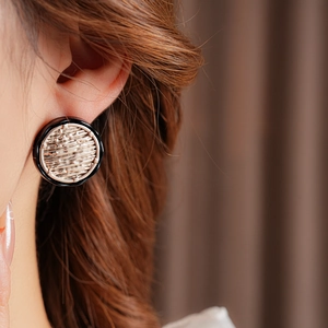 Macro shot of minimalist round gold woven earring with black border on model's ear