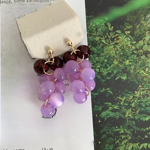 Detail of handmade grape-shaped drop earrings with purple beads and gold metal accents
