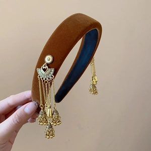 Detail of dark brown velvet headband with golden fan and bell tassel pendants