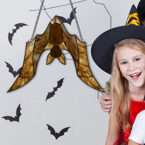 Halloween amber glass bat ornament hanging on a chain with a witch girl background