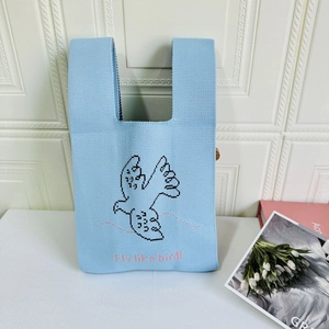 Close-up of blue knit tote bag with black bird pattern and Fly Like Bird embroidery