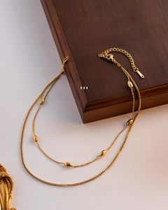 Close-up of double-layer stainless steel necklace with gold oval beads on wood box