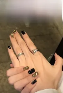 Detail of glossy black press-on nails with golden geometric accents and luxury glitter