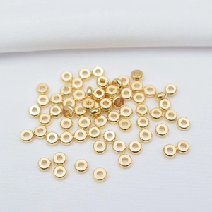 Flat lay of 14k gold-filled flat round spacer beads on a white fabric background