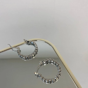 Close-up of silver geometric beaded hoop earrings reflecting on a mirror surface