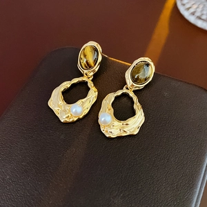 Macro detail of gold-plated textured earrings with tiger eye stone and small pearl