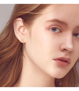 Close-up of model wearing gold butterfly stud earrings with sparkling white zircons