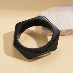 Close-up of geometric black resin hexagonal bangle on minimalist stone background