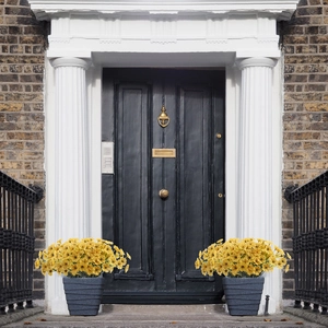 Detailed view of yellow artificial violet bouquets in textured gray pots by a door