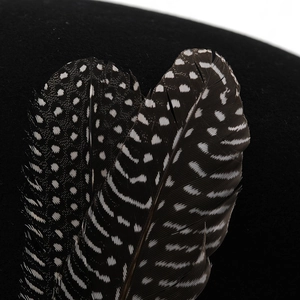 Detail of wool felt hat featuring decorative black and white patterned guinea feathers