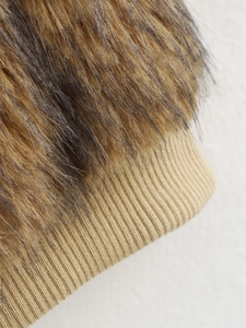 Detailaufnahme von braunem Kunstpelz und beigen Rippstrickbündchen an einem modischen Mantel