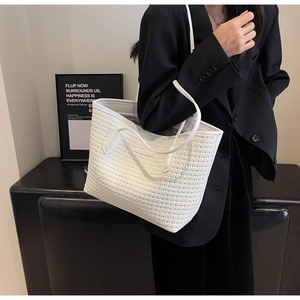 Detailed view of a white woven tote bag held by a model in a minimalist professional setting