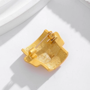 Detailed back view of golden metal mask brooch showing safety pin and textured finish
