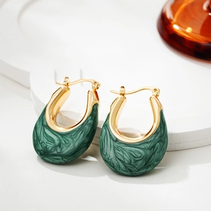Close-up of gold U-shaped earrings with dark green enamel on a marble pedestal