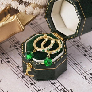 Detail of gold hoop earrings with green emerald pendants in a green velvet box