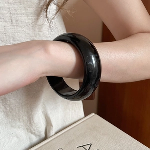 Polished wide black resin bangle bracelet for women shown on wrist in a lifestyle setting