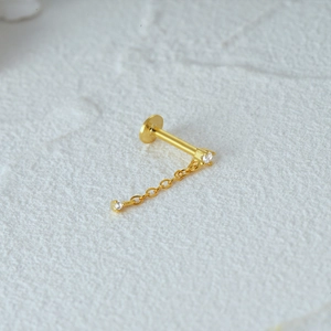 Close-up of gold cartilage stud with chain and tiny diamond in a minimalist style