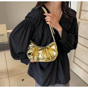 Golden pleated cloud bag styled with a black outfit in a minimalist indoor setting