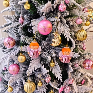 Gros plan d'ornements de Noël roses et dorés avec des anges et lunes sur un sapin enneigé