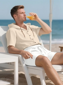 Linen set detail showing a beige hooded shirt and white drawstring shorts on the beach
