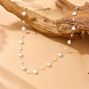 Gold-plated chain necklace with white resin hearts and pearls on a rustic wood background