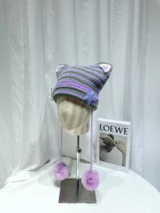 Detailed close-up of a striped cat-ear knit hat with soft purple faux fur pom-poms