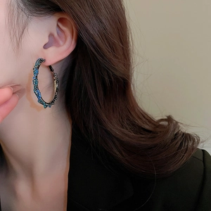 Close-up of model wearing large dark gunmetal twisted hoop earrings with blue rhinestones