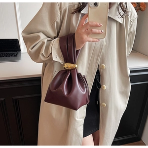 Close-up of burgundy leather bucket bag with artistic gold metal knot and pleated detail