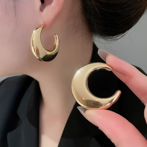 Macro detail of polished gold-tone metal C-shape hoop earrings with a mirror finish