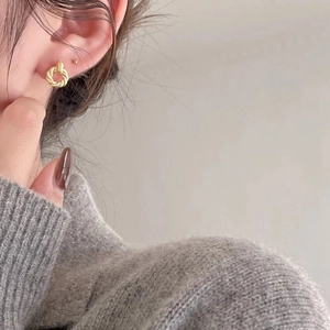 Close-up of a model wearing a golden braided texture stud earring with a glossy finish