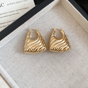 Detail of chunky gold hoop earrings with fan-shaped textured design on a jewelry tray