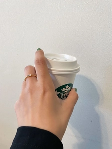 Close-up of a gold s925 silver twist ring with a rectangular zircon on a model holding a cup
